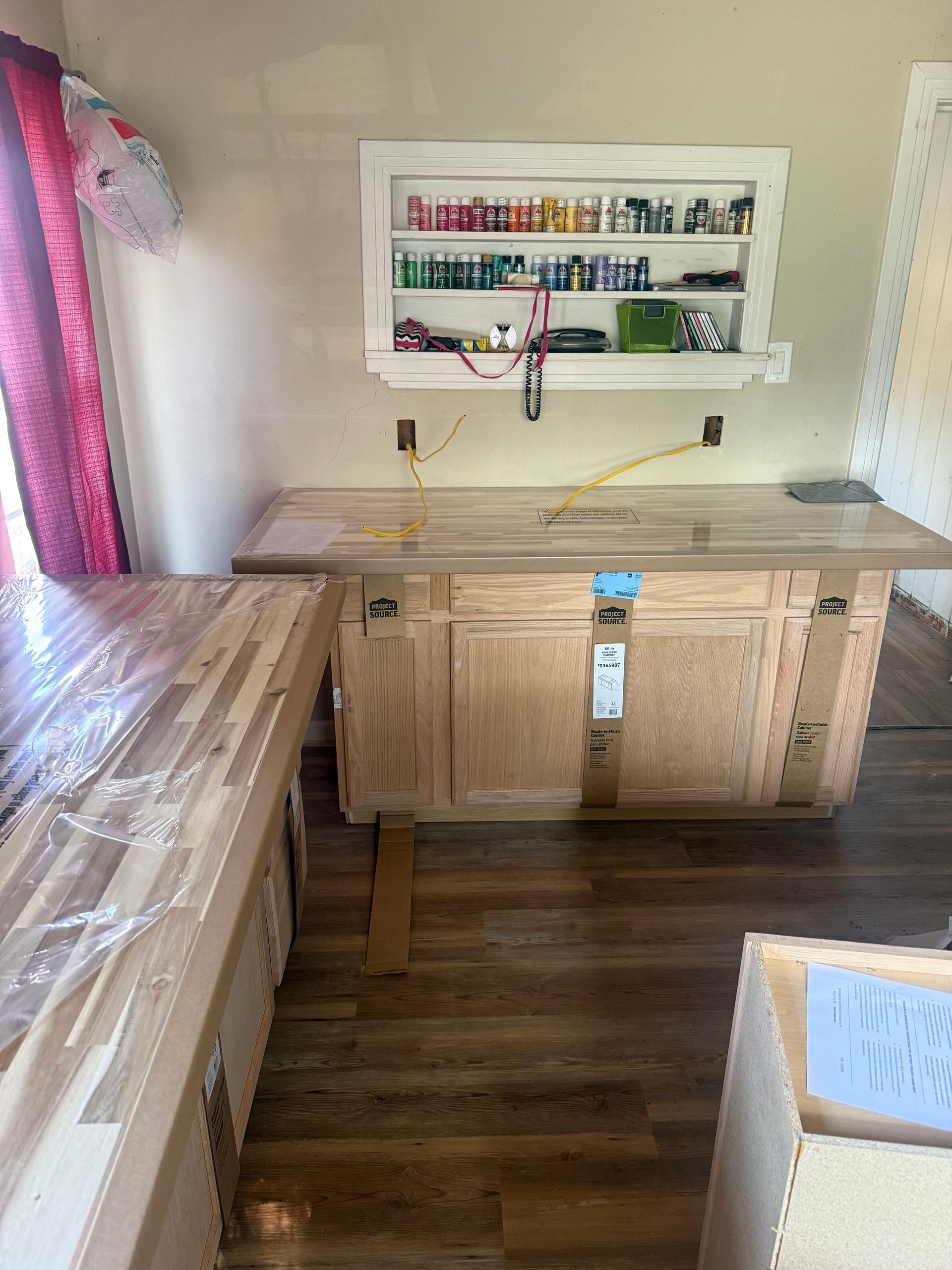 Small workshop with wooden workbench, wall shelf of supplies, and rolled material on the left.