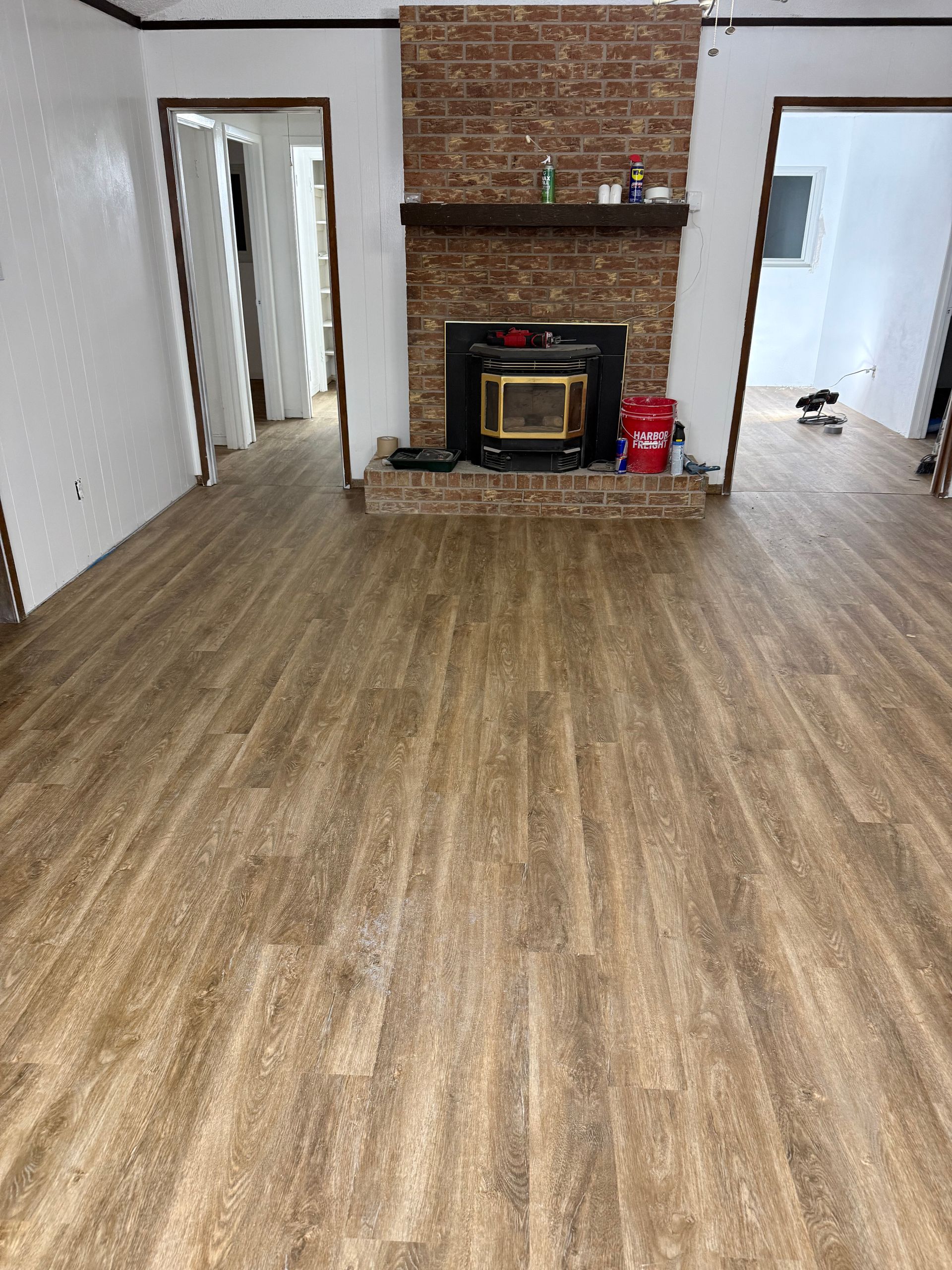 Empty living room with wood floors, brick fireplace, and doorway openings on either side