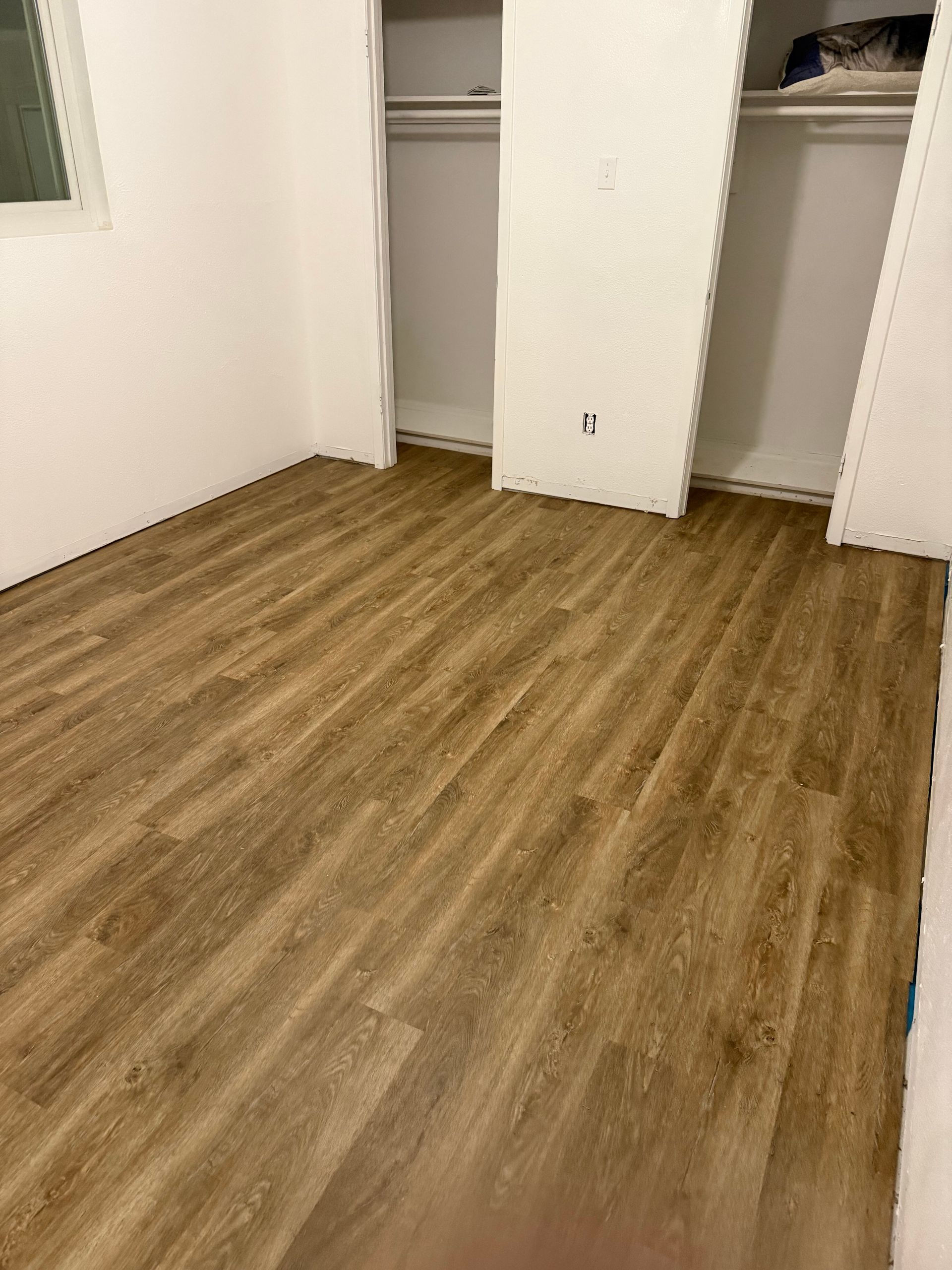 Empty room with wood flooring and open closets along the back wall.