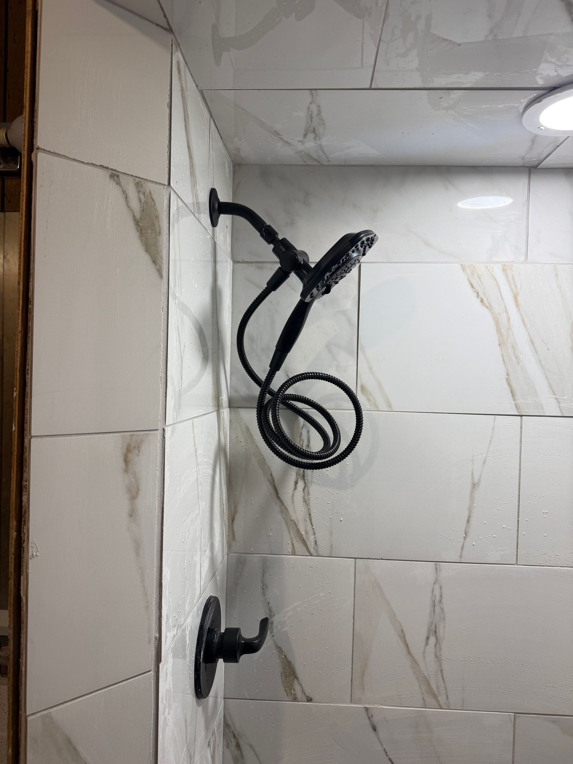 Shower stall with white marble-look tile and black shower fixtures, including a coiled hose showerhead.