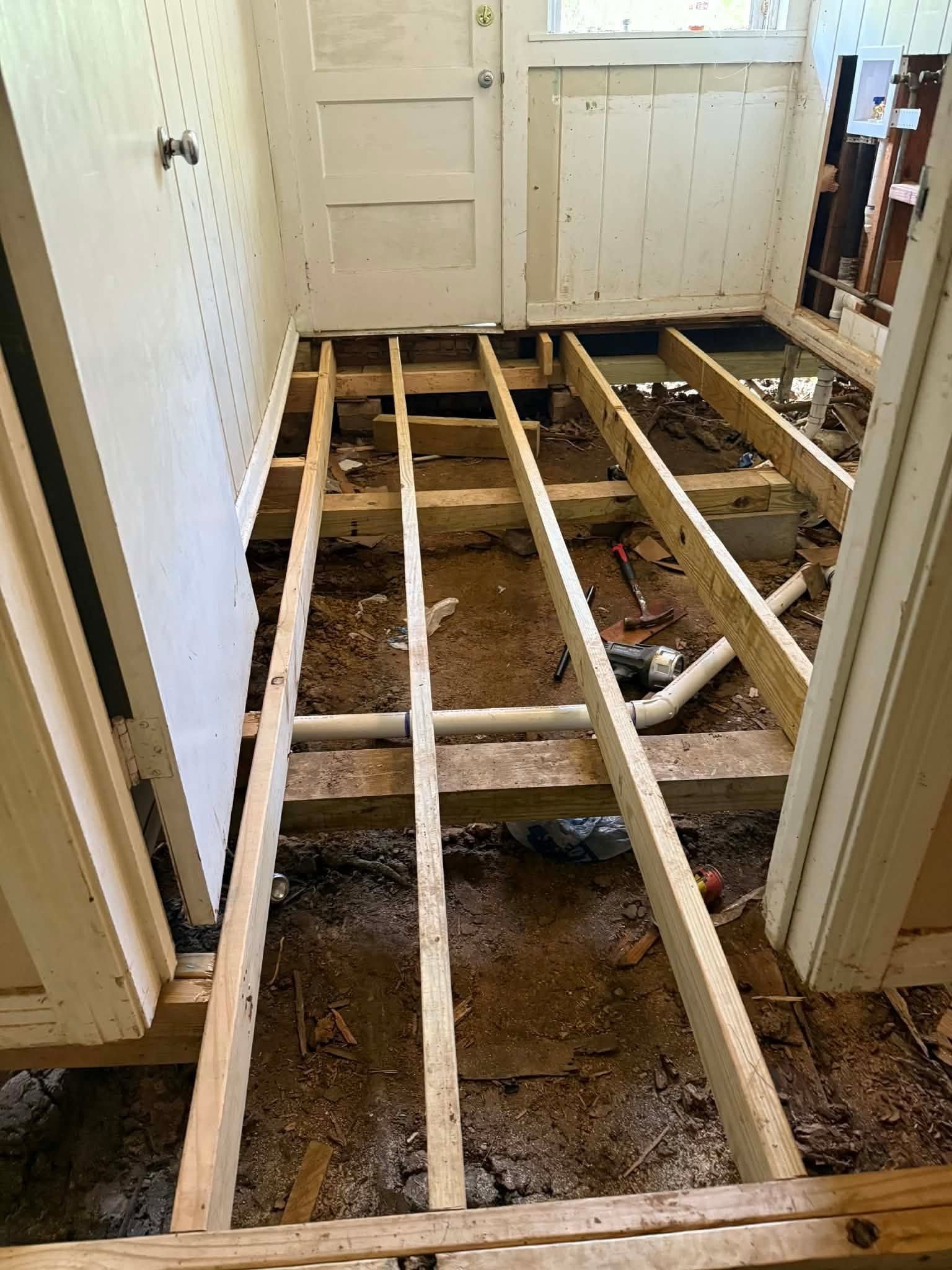 Bathroom with floorboards removed, exposing joists and subfloor framing during renovation.
