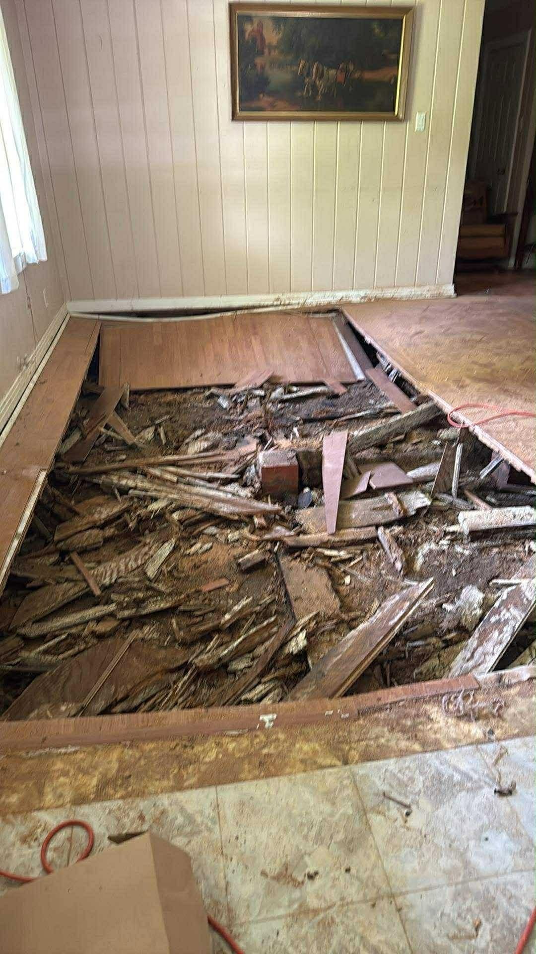 Collapsed living room floor with exposed broken joists and debris in a damaged home interior