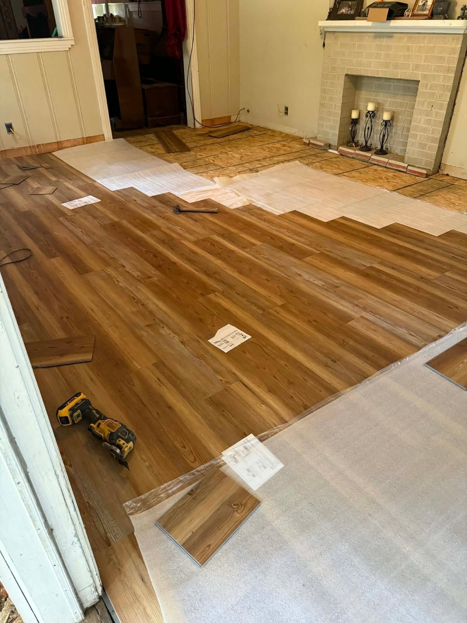 Hardwood floor installation in a living room with tools, unfinished sections, and a fireplace in the background