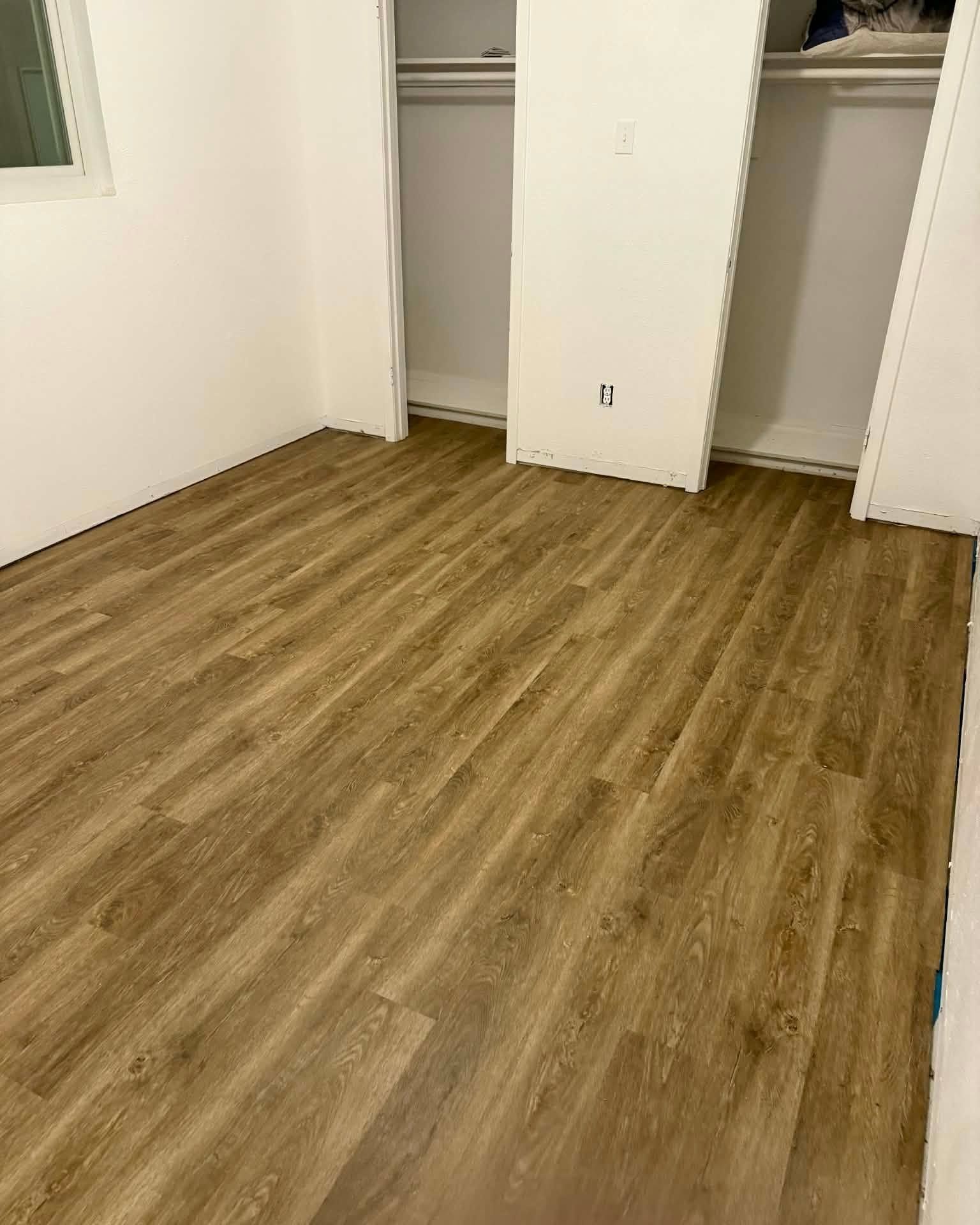 Empty bedroom with wood-look floor and open closet doors.