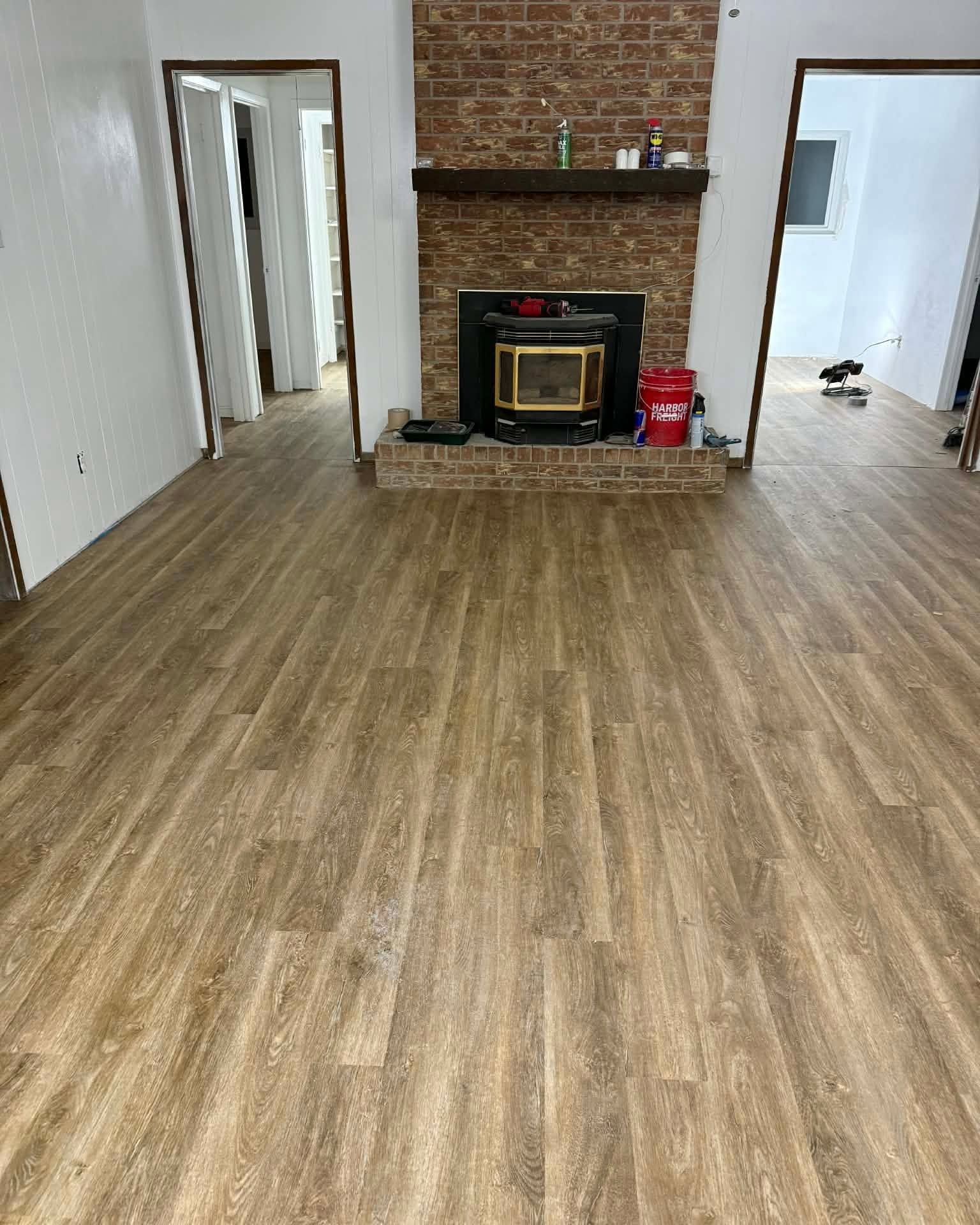 Empty room with wood-look flooring, brick fireplace, and white walls with doorways on both sides