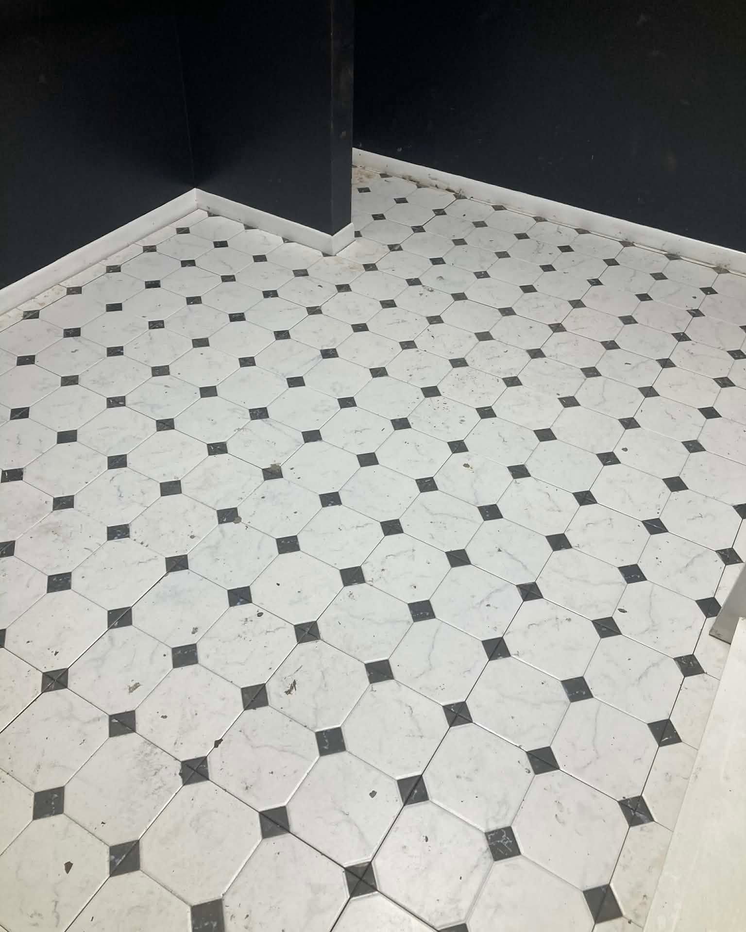 White-and-black patterned tiled floor in a corner of a room with dark walls