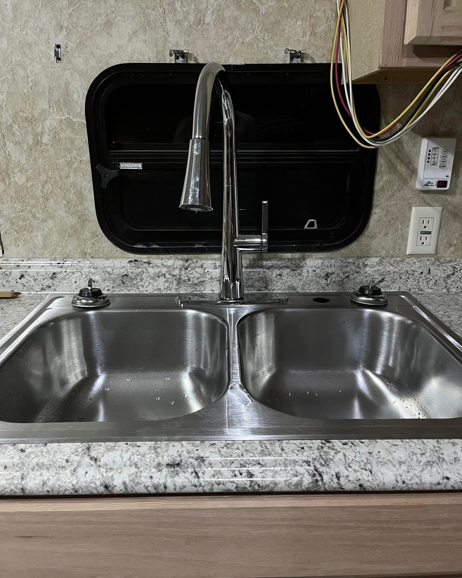 Stainless steel double sink with chrome faucet under a black window in a granite countertop kitchen area