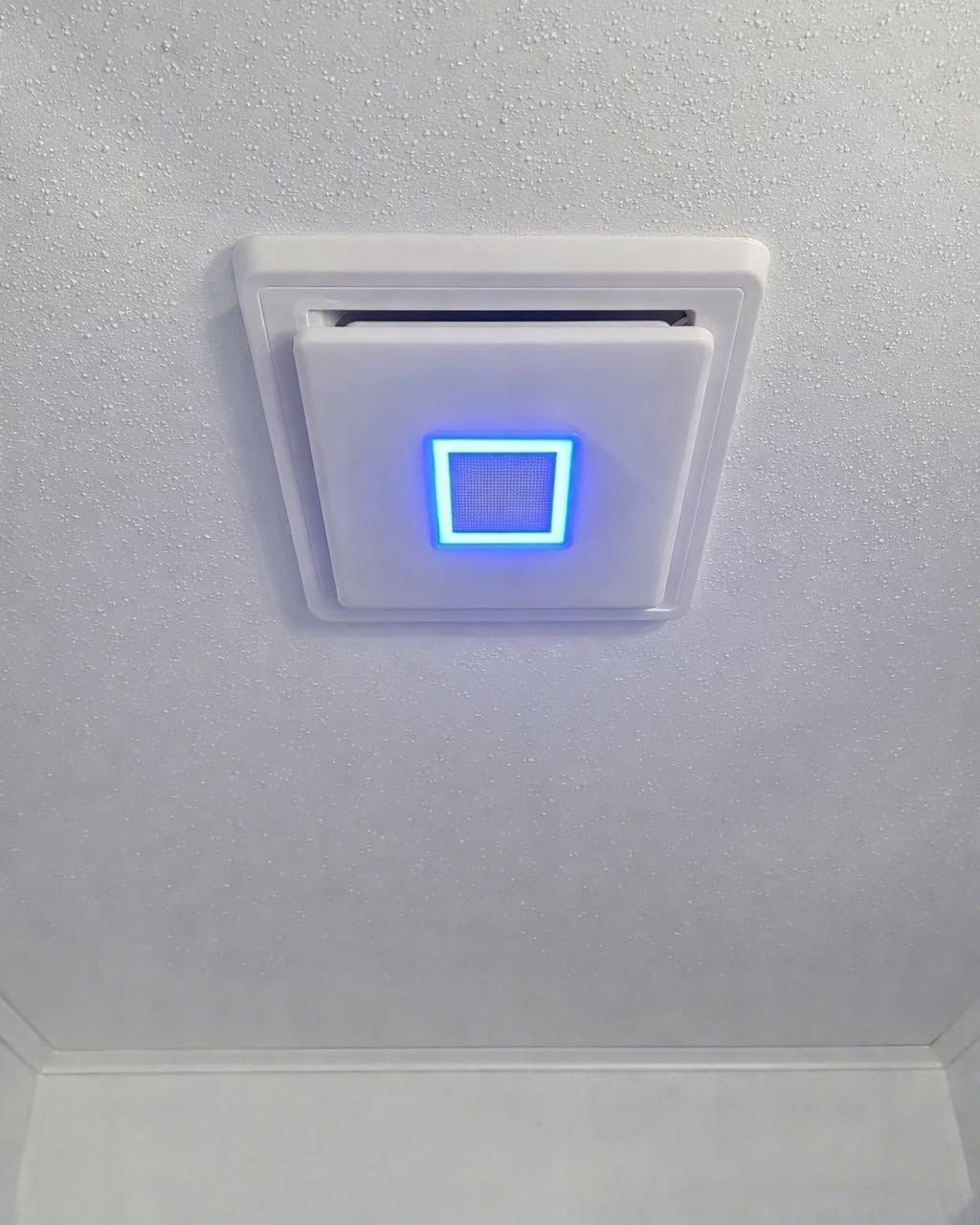 Ceiling vent with a glowing blue light in a white room