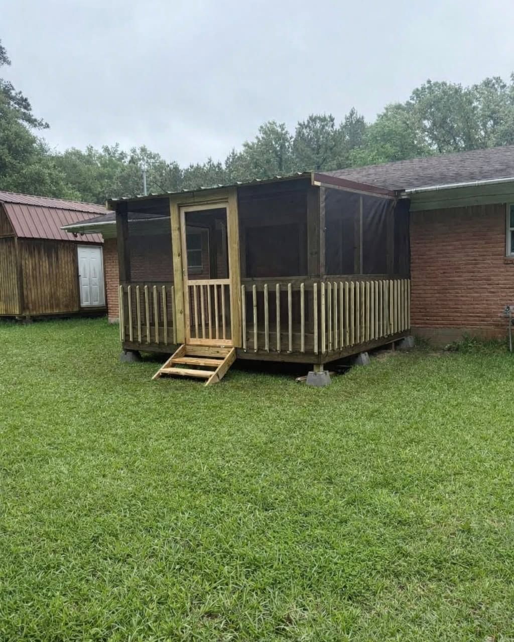 Small wooden porch with steps attached to a brick house, set on a grassy yard under an overcast sky