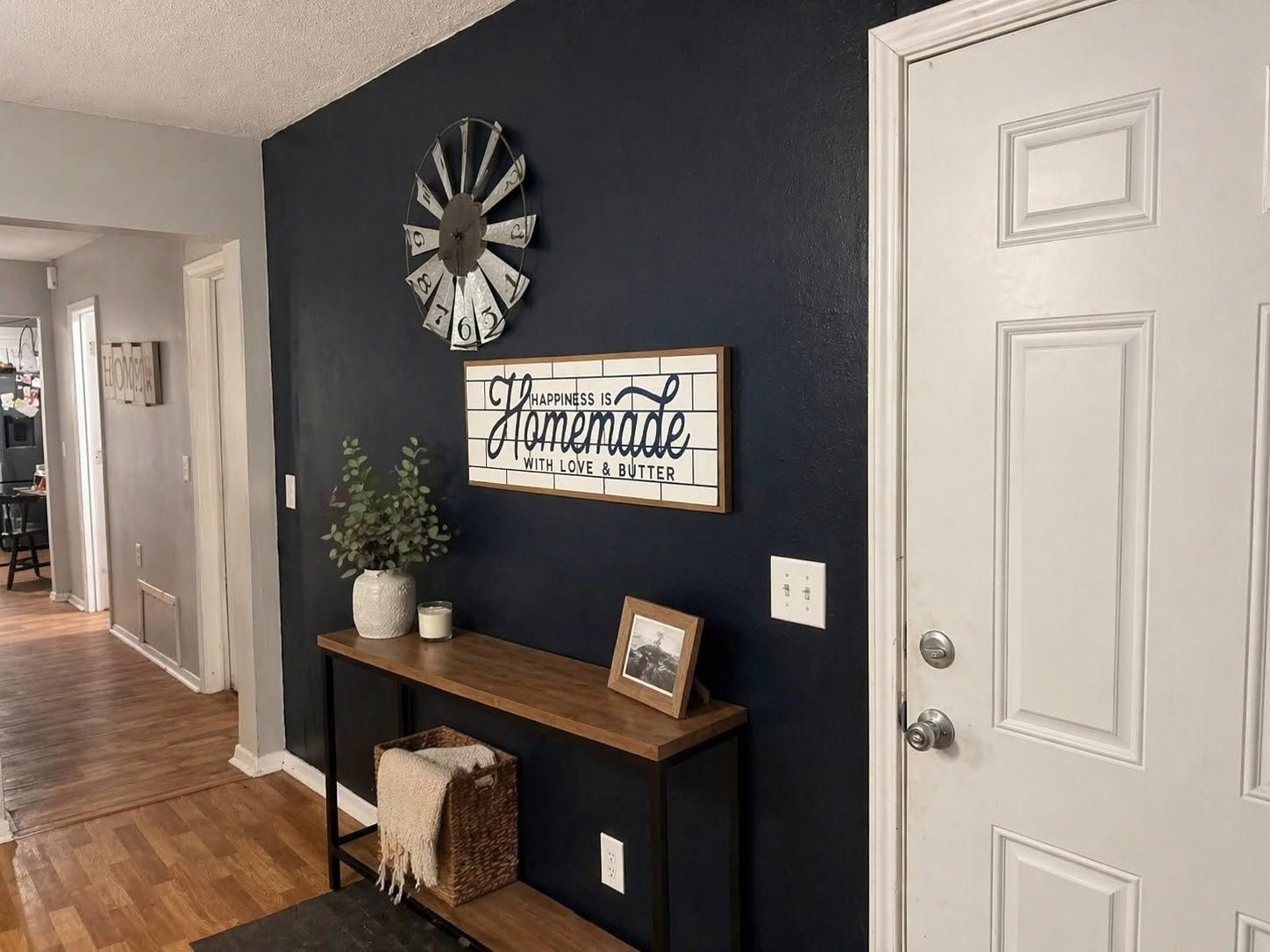 Hallway with navy accent wall, decorative clock, wall art, console table, and white door.