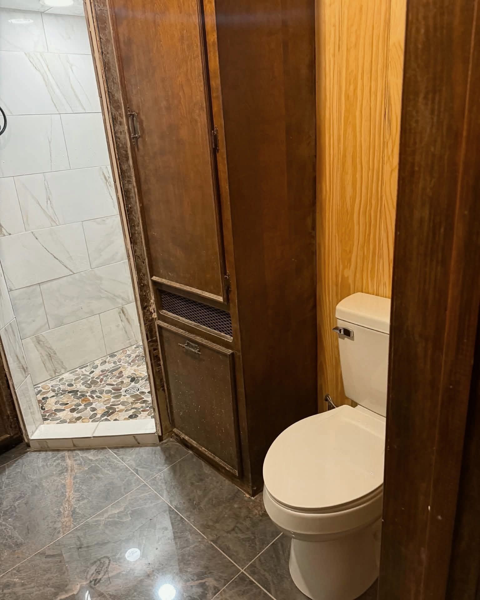 Small bathroom with a toilet beside a wooden door and tiled floor.