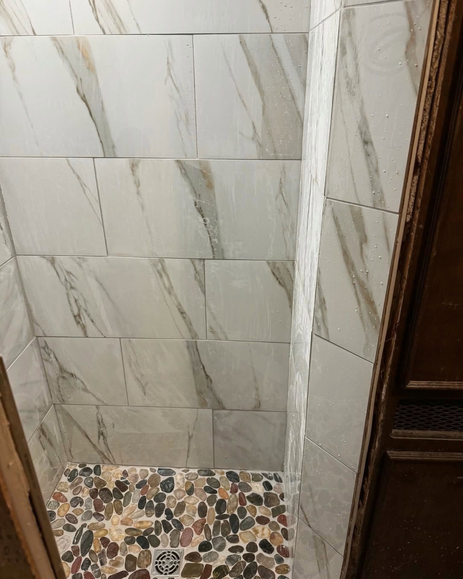 Tiled shower corner with white wall tiles and a colorful mosaic floor