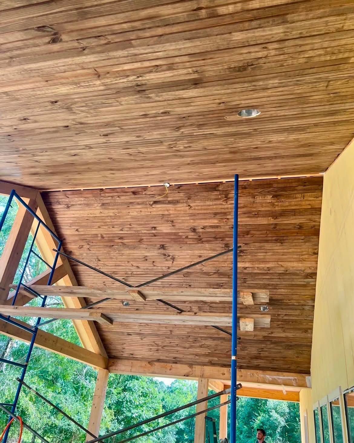 Wooden ceiling and blue support poles on a partially built outdoor structure, with green trees beyond