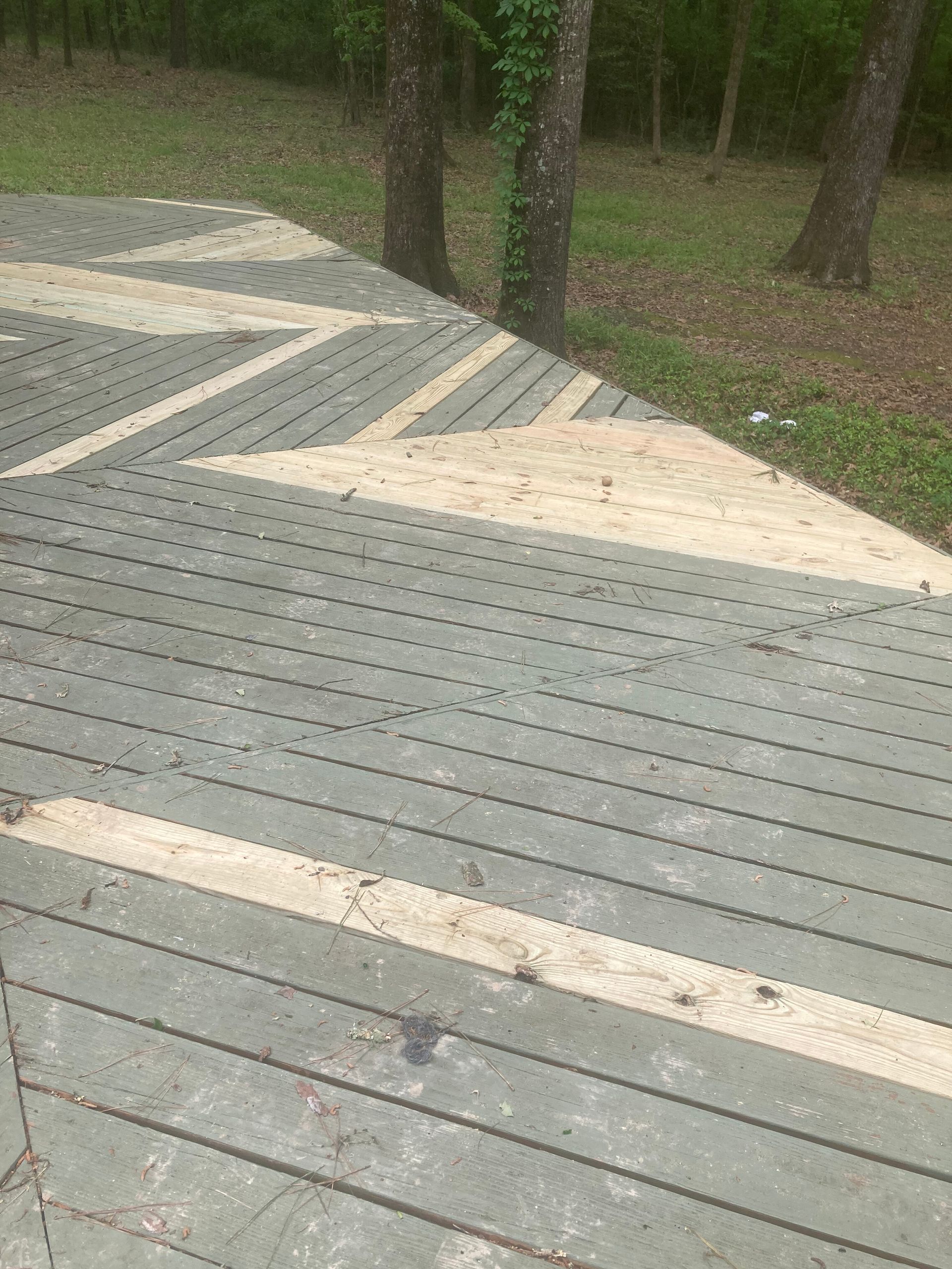 Wooden boardwalk with pale diagonal paving strips beside trees and grass in a park