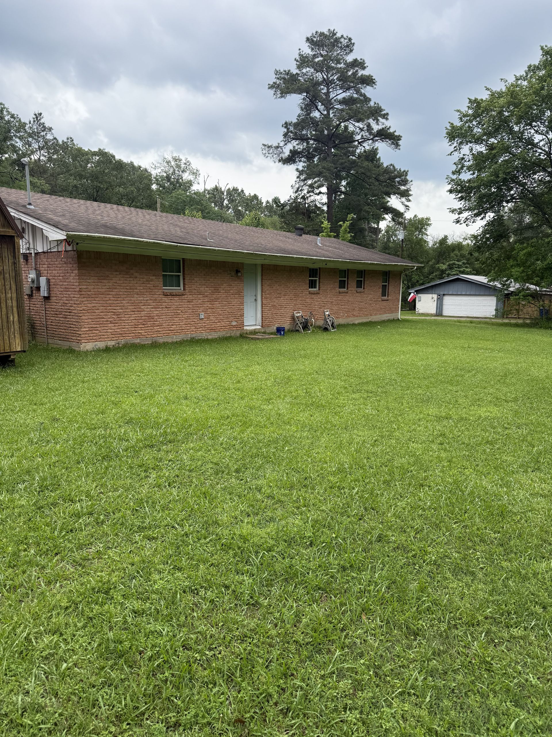 Single-story brick house with a tiled roof beside a large grassy yard and detached garage.
