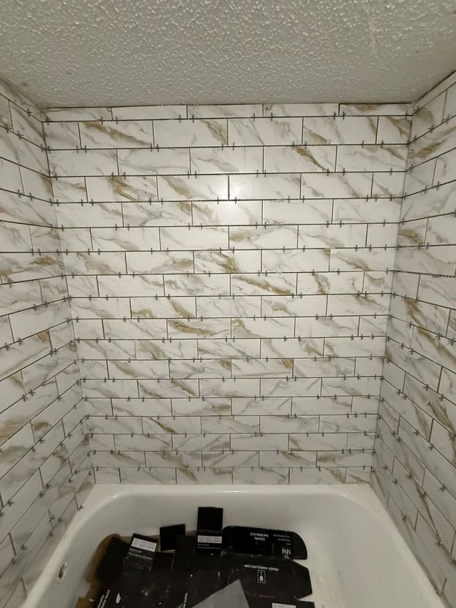 Bathtub with marble tile walls and a cluster of dark bottles at the bottom