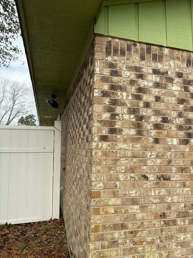Brick house corner with green eaves, white gate, and side yard grass.