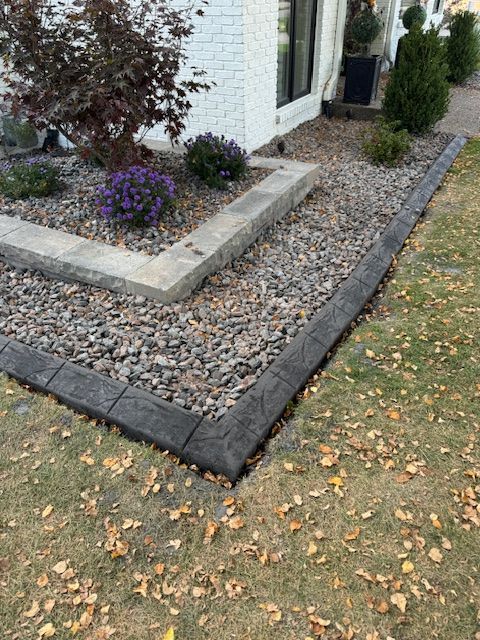 A concrete curb with gravel and flowers in front of a house.