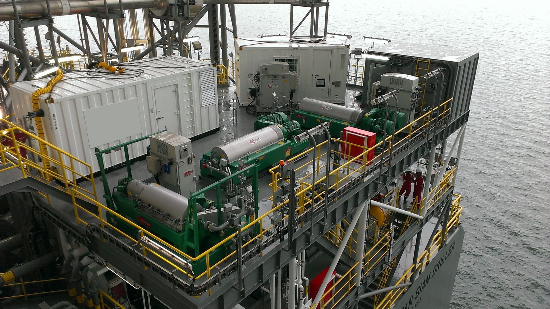 Offshore industrial platform with green machinery and yellow railings beside open water