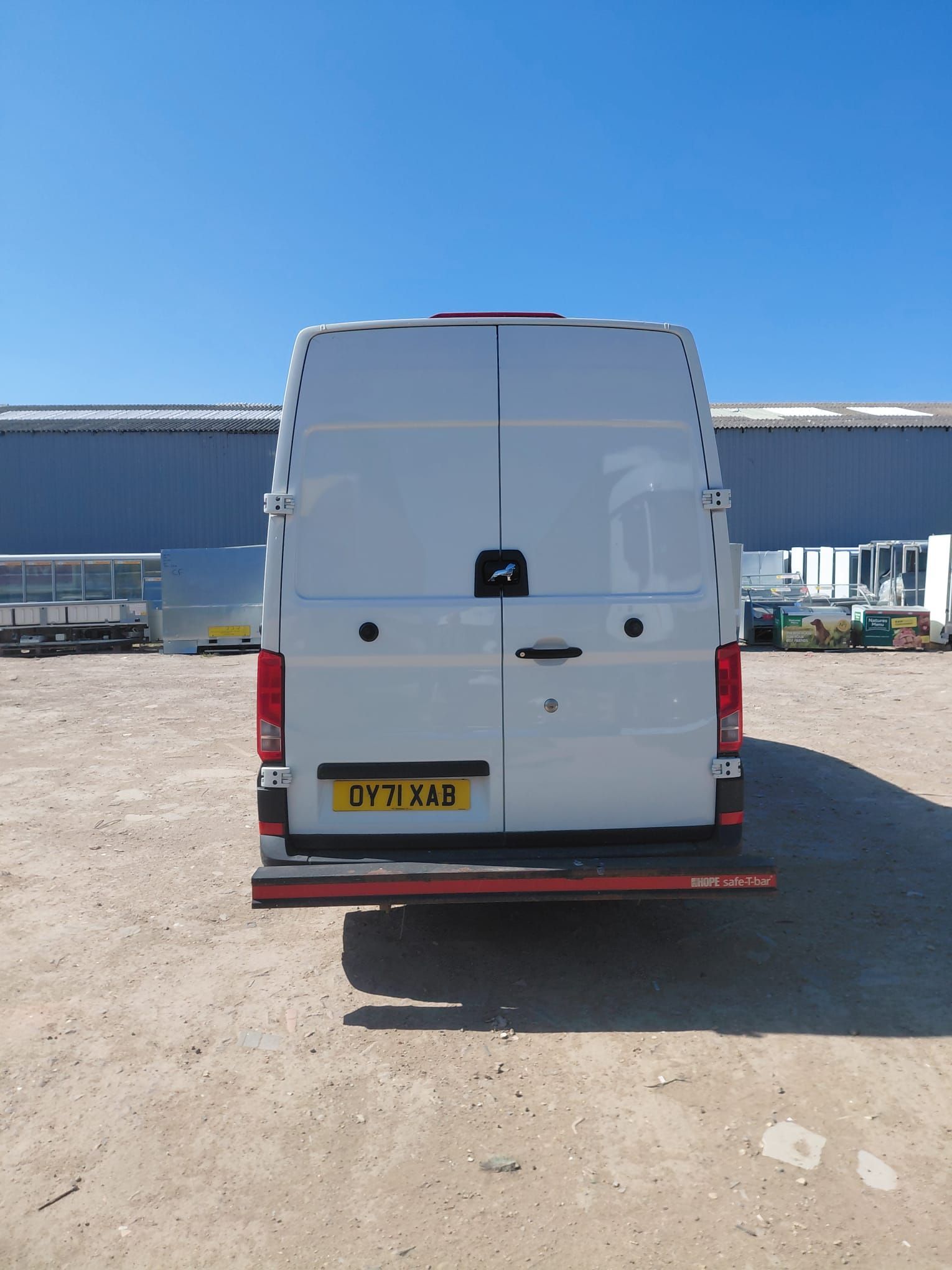 Rear view of a white cargo van parked on a dusty lot under a clear blue sky.