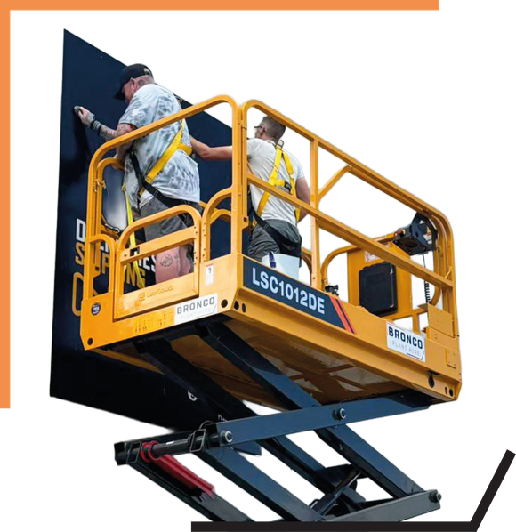 Two workers on a yellow scissor lift painting a large dark wall outdoors