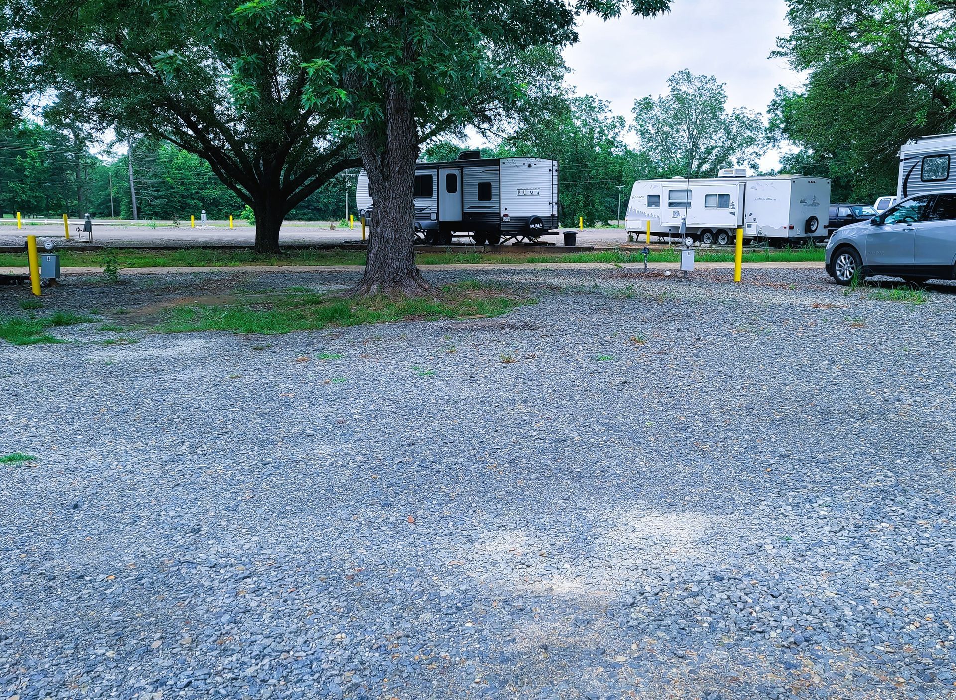 A car is parked in a gravel lot next to a rv.