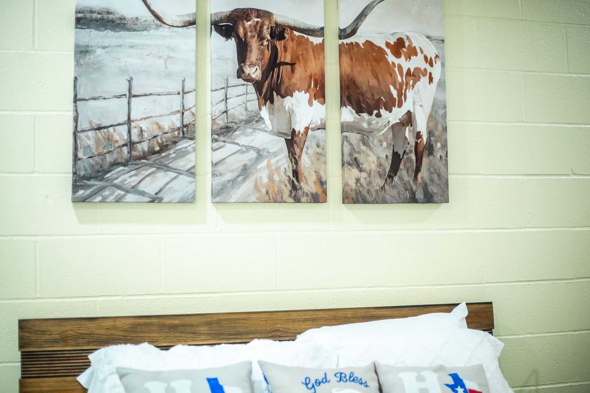 Three paintings of a longhorn cow are hanging on a wall above a bed.