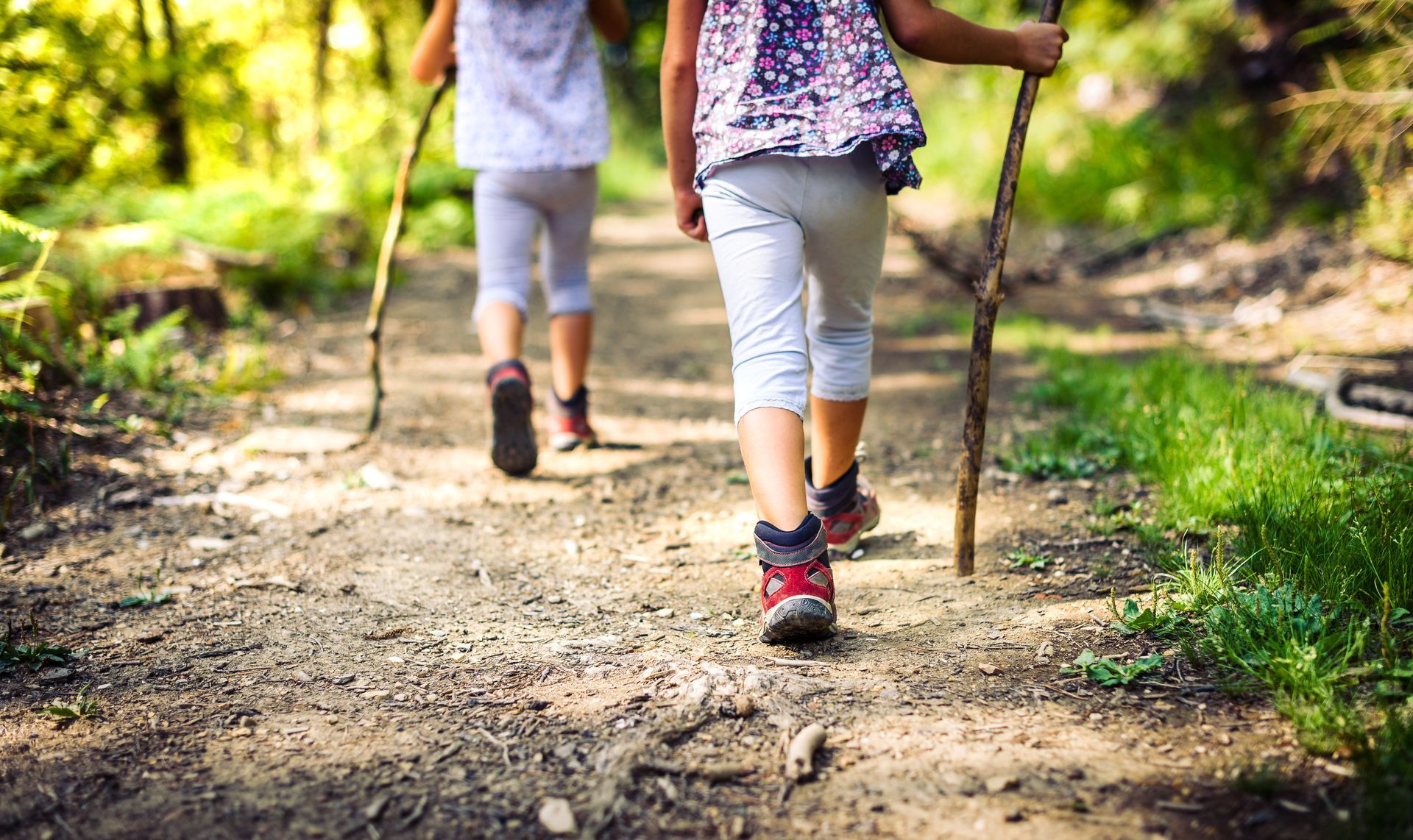 Two little girls are walking down a dirt path in the woods.