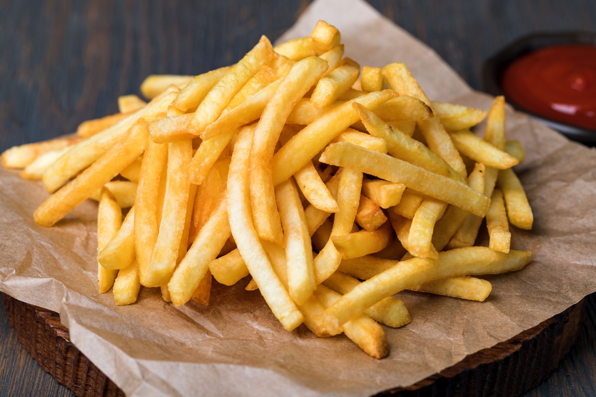 A pile of french fries on a piece of paper next to a bowl of ketchup.