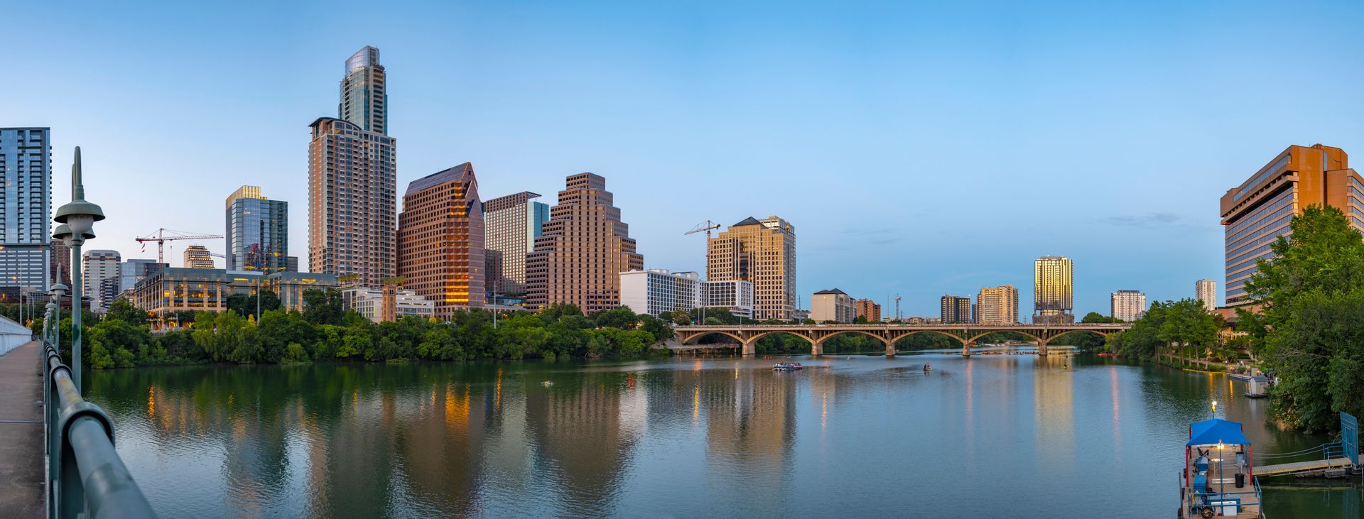 A city skyline with a river in the foreground and a bridge in the background.
