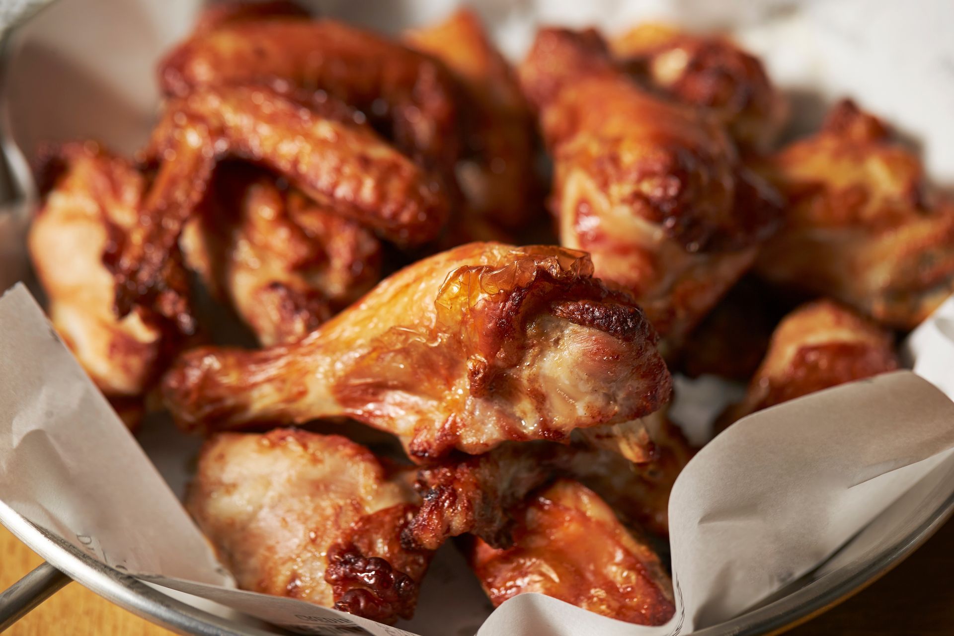 A bowl of chicken wings is sitting on a wooden table.