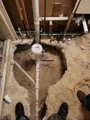 Open floor around exposed white plumbing pipes and a drain in a rough utility area.