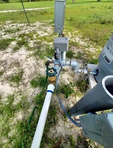 Utility meter and pipe assembly beside an HVAC unit on a grassy outdoor lot.