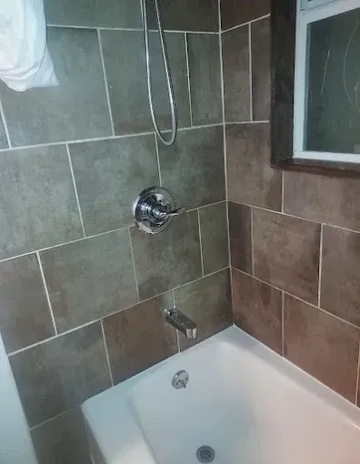 Tiled bathroom shower-tub with chrome fixtures and a window