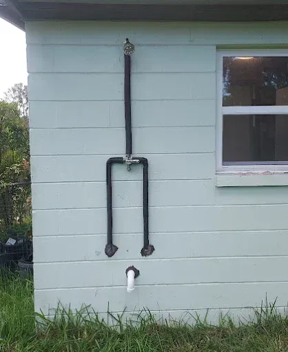 Black pipes mounted on a pale green house exterior beneath a window.