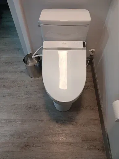 Modern white toilet in a bathroom with gray flooring and a small metal trash can nearby