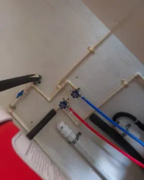 Red, blue, and black hoses connected to wall-mounted plumbing pipes near a white tank.