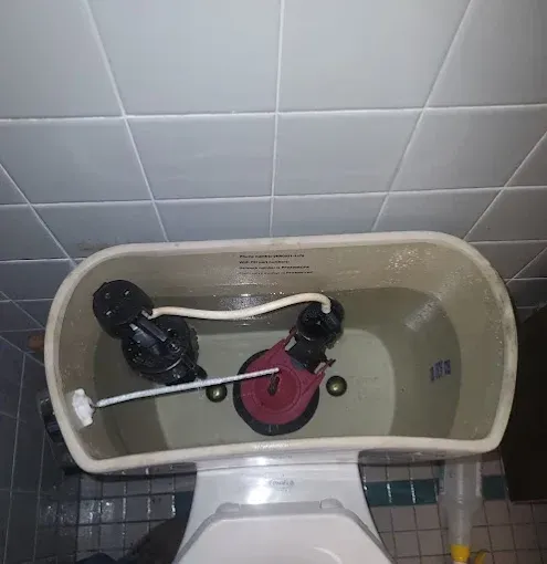 Open toilet tank with black and pink flush parts inside against white tiled wall