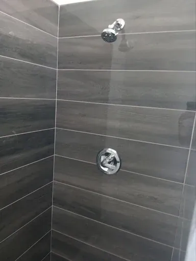 Gray tiled shower stall with showerhead and control valve on the wall