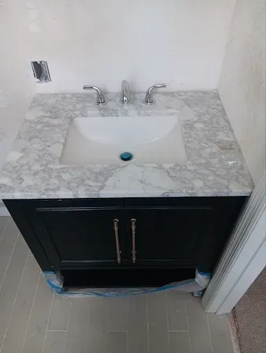 Marble vanity with white sink and chrome faucet, black cabinet below, in a small bathroom.