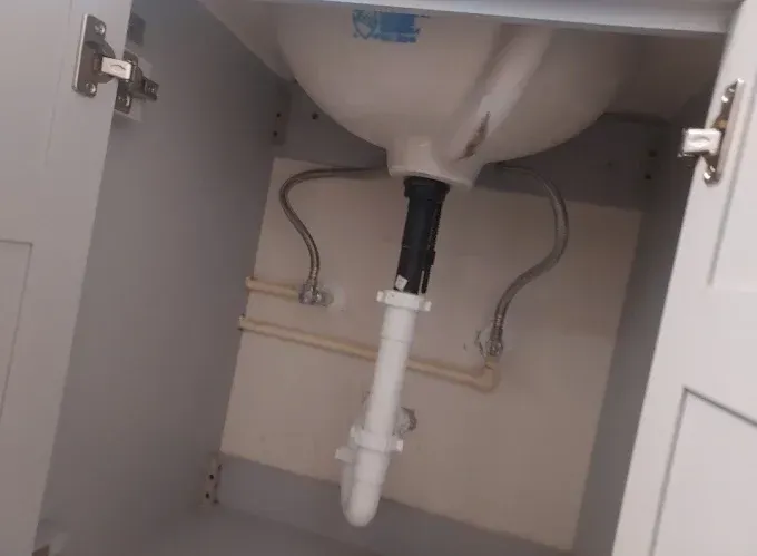 Open cabinet under a sink showing plumbing pipes and drain trap