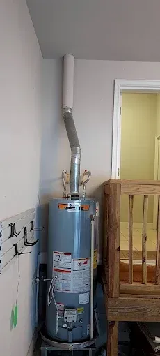 Water heater with metal vent pipe installed in a utility room next to a wooden railing.