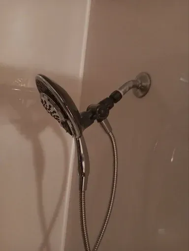 Handheld showerhead mounted on a beige tiled bathroom wall.