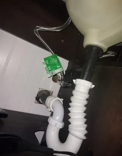 Under-sink plumbing with white drain pipes, black hose, and a green disposer/disconnect fitting