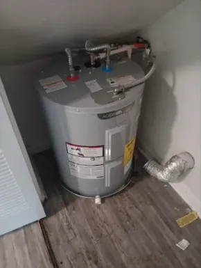 Water heater in a utility closet with pipes and vents on a wood floor.
