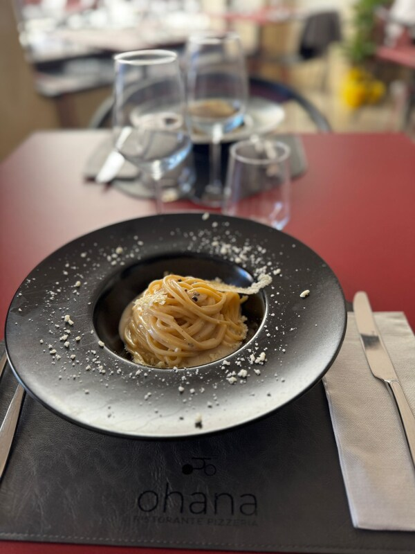 Piatto di pasta in una ciotola nera, guarnito con formaggio grattugiato, su un tavolo rosso in un ristorante.