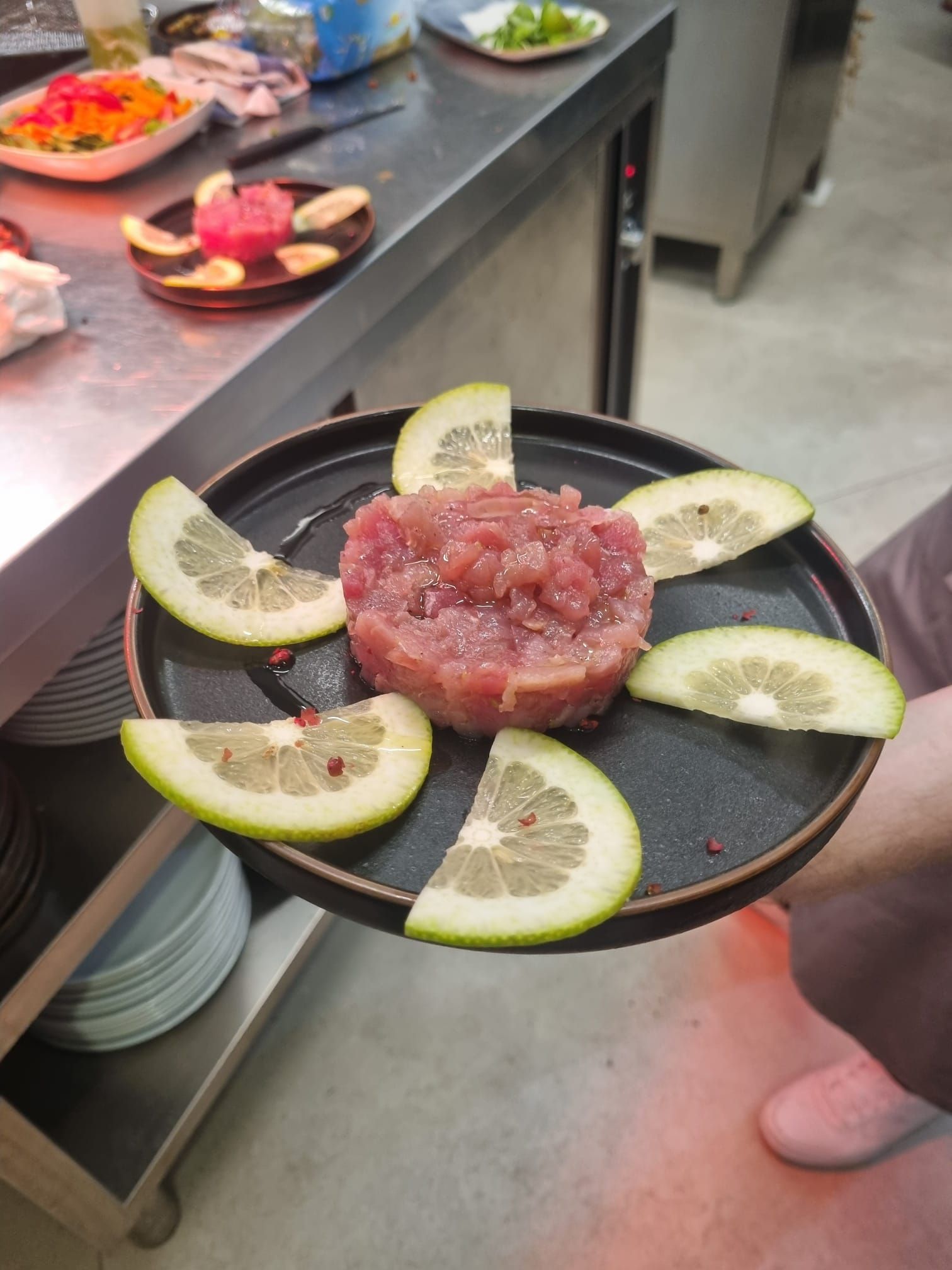 Un piatto di tartare di tonno con fette di pompelmo, tenuto in mano da una persona in cucina.