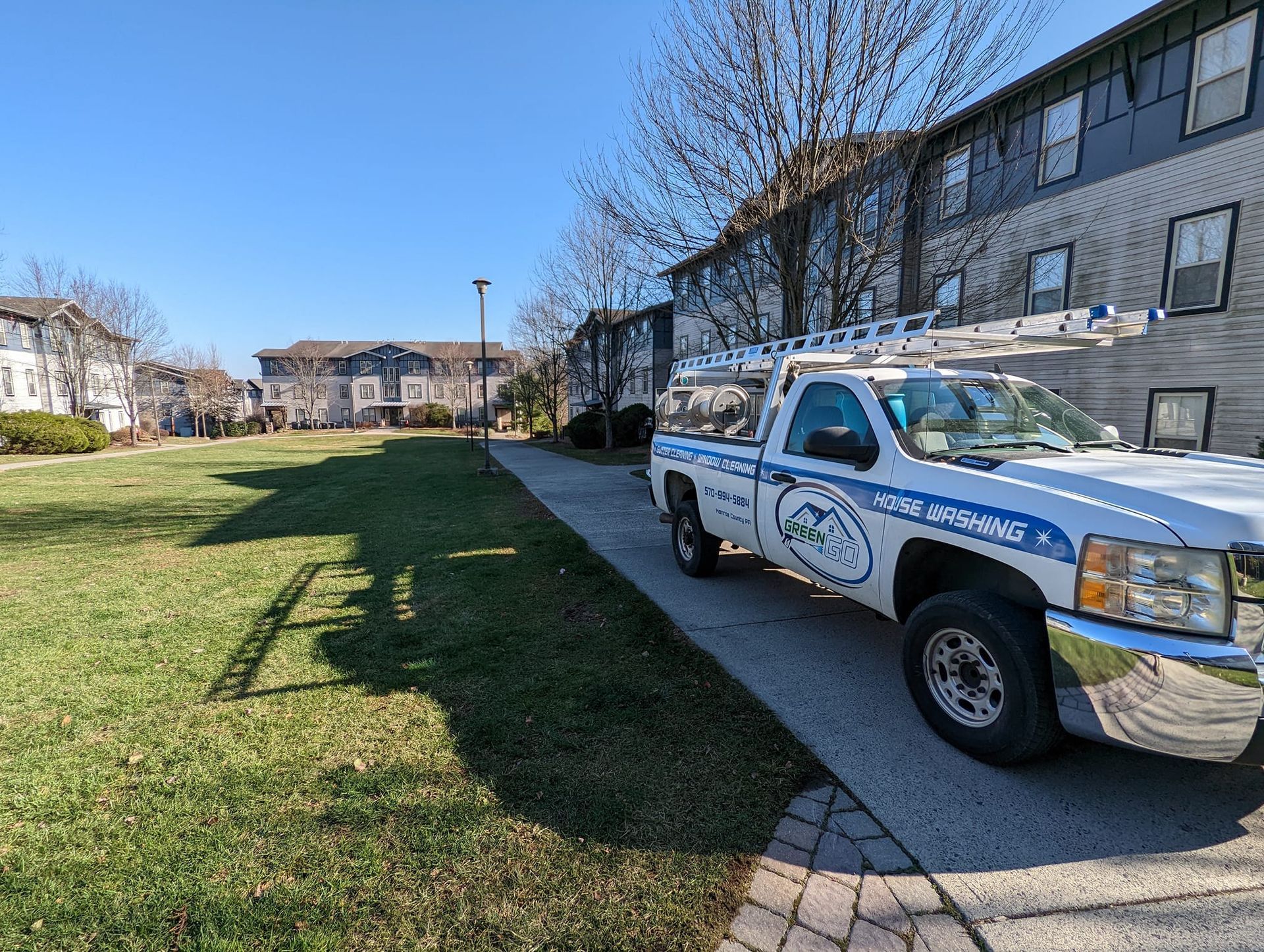 White work truck parked beside a paved path in front of a multi-story building.