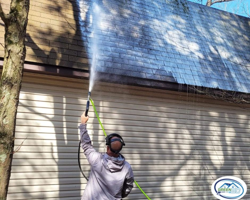 Man power washing a roof with a hose; spraying water upwards.