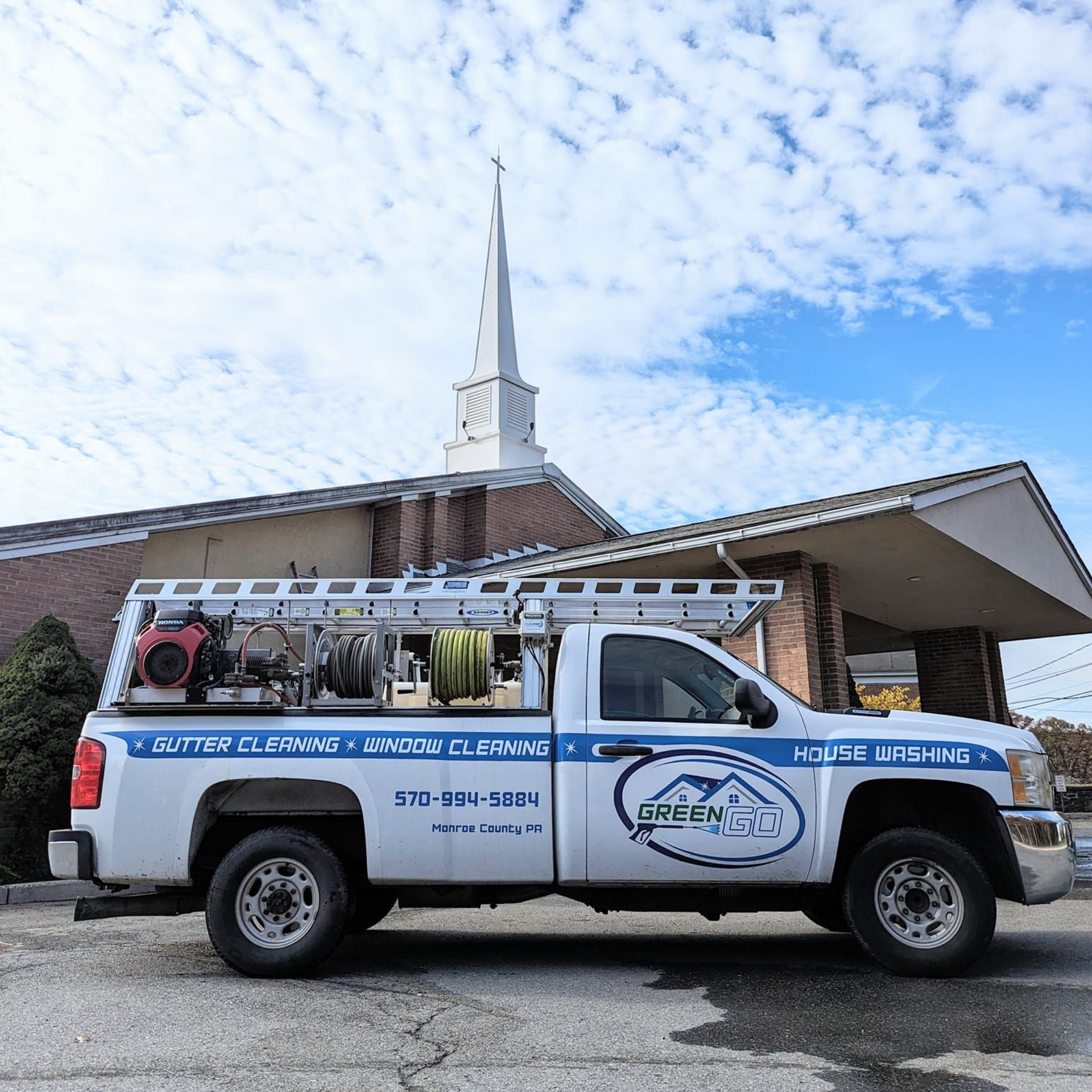White truck with cleaning equipment parked near a brick church with a steeple.